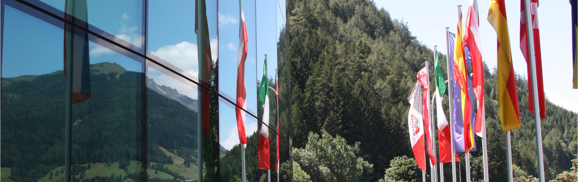 Sede centrale di MALTECH con facciata in vetro, bandiere nazionali e paesaggio montano.